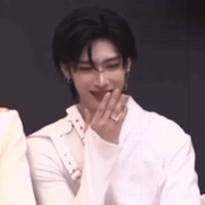 A Man In A White Shirt Is Covering His Mouth With His Hand While Sitting Next To Another Man . GIF