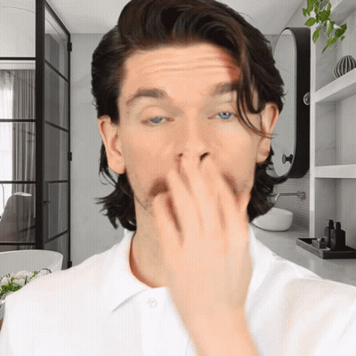 A Man In A White Shirt Is Covering His Nose With His Hand GIF