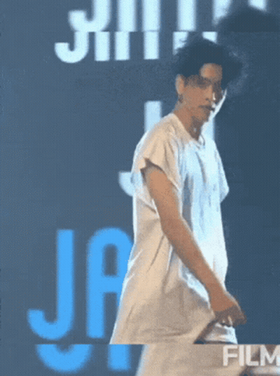 A Man In A White Shirt Is Dancing In Front Of A Blue Sign That Says Film GIF