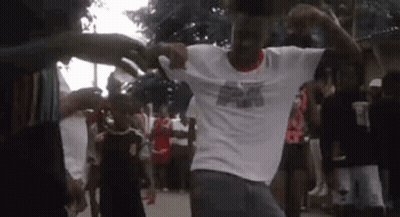 A Man In A White Shirt Is Dancing In Front Of A Crowd . GIF
