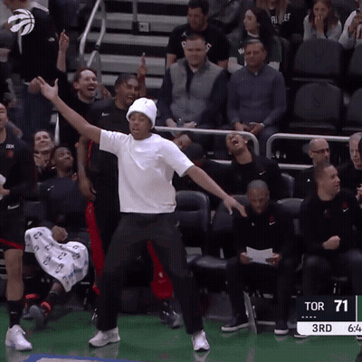 A Man In A White Shirt Is Dancing In Front Of A Crowd At A Sports Game GIF