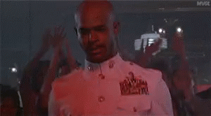A Man In A White Shirt Is Dancing In Front Of A Crowd In A Red Light . GIF