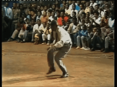 A Man In A White Shirt Is Dancing In Front Of A Crowd Of People GIF