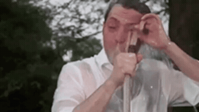 A Man In A White Shirt Is Drinking From A Straw . GIF