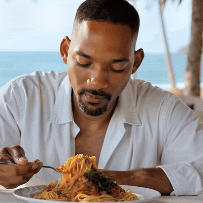 A Man In A White Shirt Is Eating A Plate Of Spaghetti With A Fork GIF