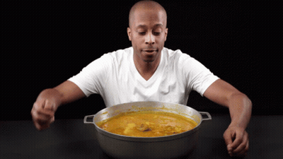 A Man In A White Shirt Is Eating From A Large Pot GIF