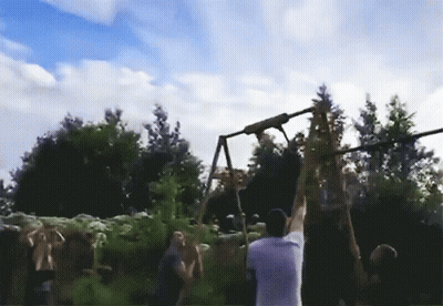 A Man In A White Shirt Is Hanging From A Rope In Front Of A Crowd Of People GIF