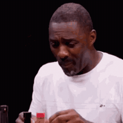 A Man In A White Shirt Is Holding A Bottle Of Hot Sauce In His Hand . GIF