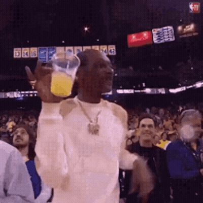 A Man In A White Shirt Is Holding A Glass Of Orange Juice In His Hand GIF