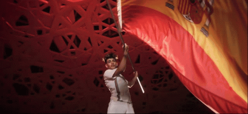 A Man In A White Shirt Is Holding A Large Red And Gold Flag GIF