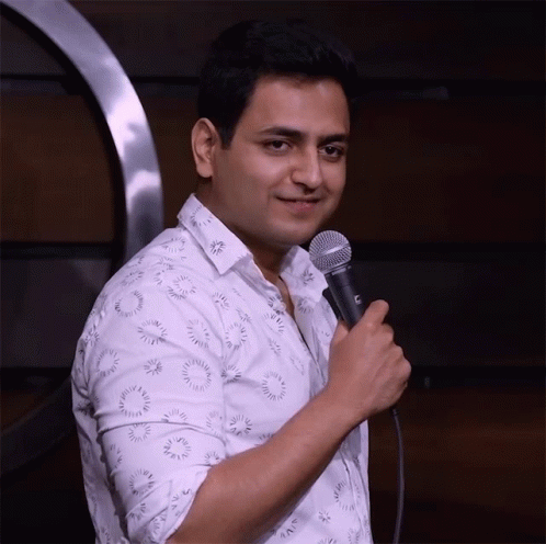 A Man In A White Shirt Is Holding A Microphone With A C On It GIF