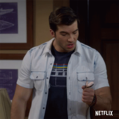 A Man In A White Shirt Is Holding A Pair Of Glasses And A Netflix Logo Is Behind Him GIF