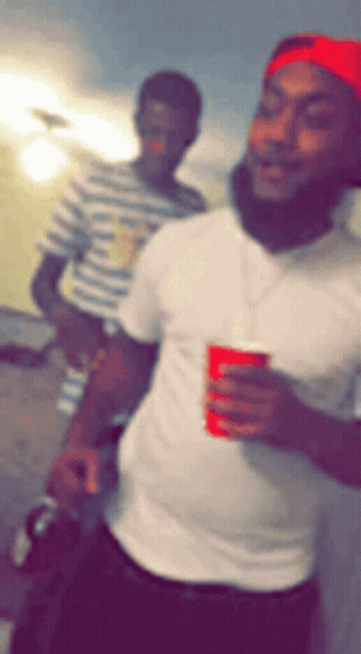 A Man In A White Shirt Is Holding A Red Cup And Smiling GIF