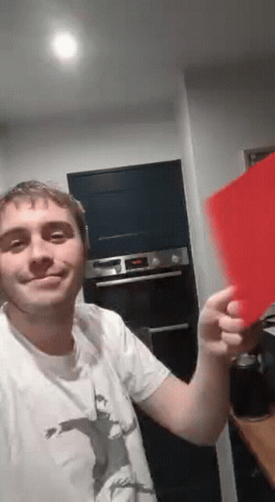 A Man In A White Shirt Is Holding A Red Piece Of Paper In His Hand . GIF