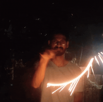 A Man In A White Shirt Is Holding A Sparkler In The Dark GIF