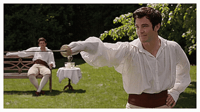 A Man In A White Shirt Is Holding A Sword In Front Of Another Man Sitting On A Bench GIF