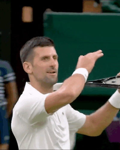 A Man In A White Shirt Is Holding A Tennis Racket In His Hand GIF