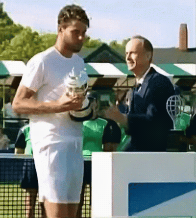 A Man In A White Shirt Is Holding A Trophy And Talking To Another Man In A Suit GIF