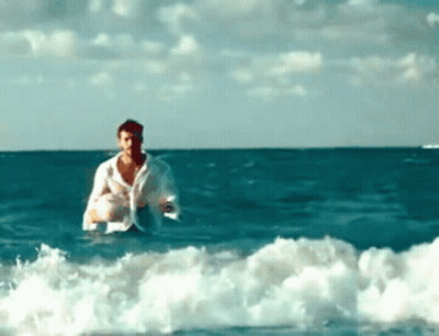 A Man In A White Shirt Is In The Ocean GIF