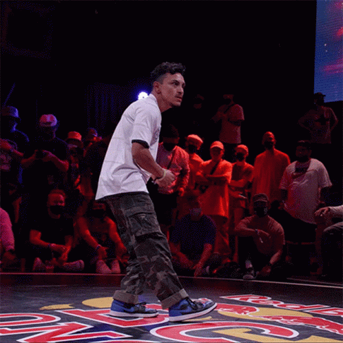 A Man In A White Shirt Is Jumping In The Air In Front Of A Crowd That Is Watching GIF