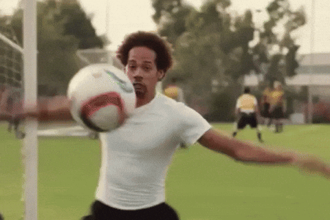A Man In A White Shirt Is Kicking A Soccer Ball On A Field GIF