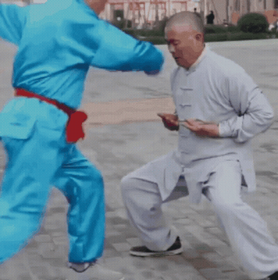 A Man In A White Shirt Is Kicking Another Man In A Blue Outfit GIF