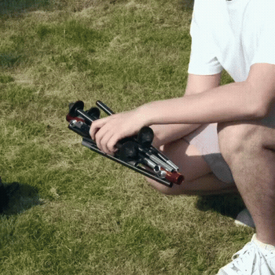 A Man In A White Shirt Is Kneeling Down In The Grass Holding A Folding Stool GIF