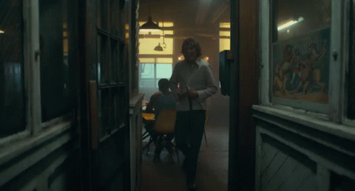 A Man In A White Shirt Is Laughing While Standing In Front Of A Window GIF