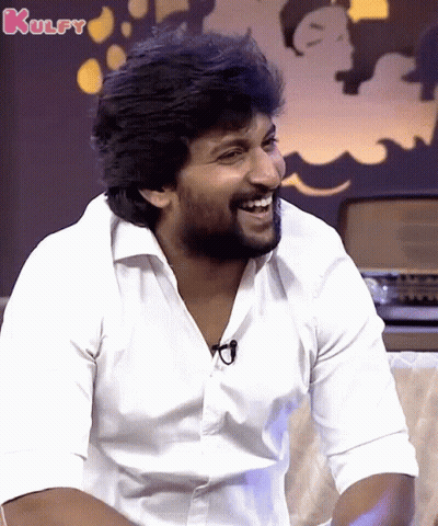 A Man In A White Shirt Is Laughing With The Word Kulfy In The Background GIF