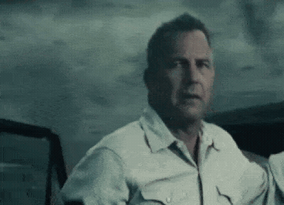 A Man In A White Shirt Is Looking Out Of A Car Window . GIF