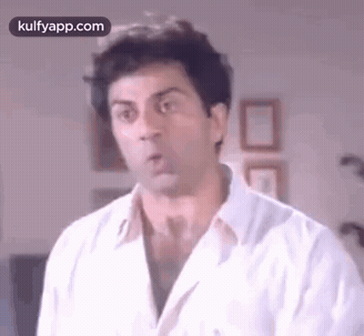 A Man In A White Shirt Is Making A Funny Face And Looking At The Camera . GIF