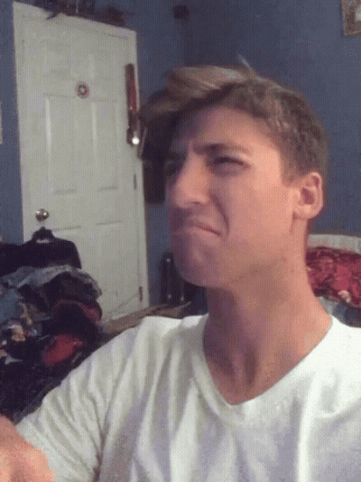 A Man In A White Shirt Is Making A Funny Face In Front Of A Door GIF