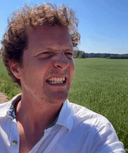 A Man In A White Shirt Is Making A Funny Face In Front Of A Green Field GIF
