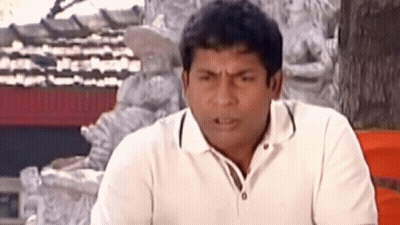 A Man In A White Shirt Is Making A Funny Face While Sitting In Front Of A Statue . GIF