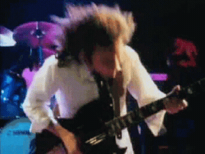 A Man In A White Shirt Is Playing A Guitar In Front Of A Drum Set GIF