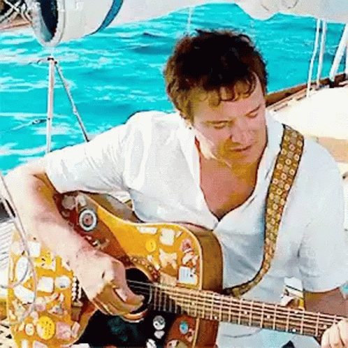 A Man In A White Shirt Is Playing A Guitar On A Boat . GIF