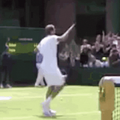 A Man In A White Shirt Is Playing Tennis On A Green Court GIF