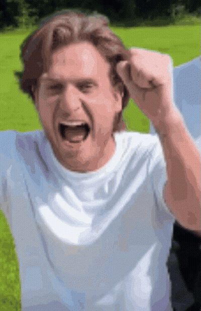 A Man In A White Shirt Is Raising His Fist In The Air . GIF