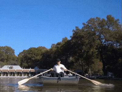 A Man In A White Shirt Is Rowing A Boat In A Lake GIF