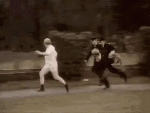 A Man In A White Shirt Is Running Away From Two Police Officers Who Are Chasing Him . GIF