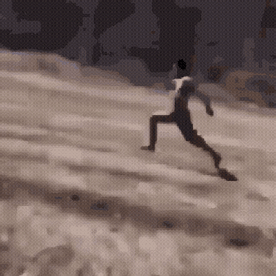 A Man In A White Shirt Is Running On A Sandy Hill GIF
