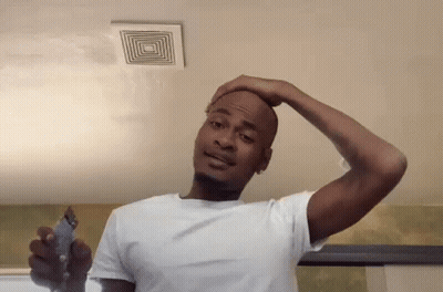 A Man In A White Shirt Is Shaving His Head With A Trimmer . GIF