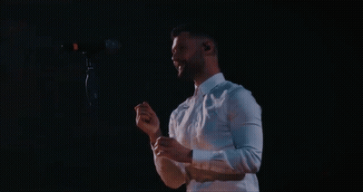 A Man In A White Shirt Is Singing Into A Microphone In A Dark Room GIF