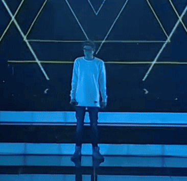 A Man In A White Shirt Is Singing Into A Microphone On Stage GIF