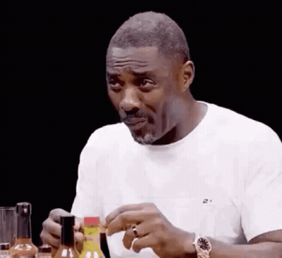 A Man In A White Shirt Is Sitting At A Table With A Bottle Of Hot Sauce In His Hand . GIF