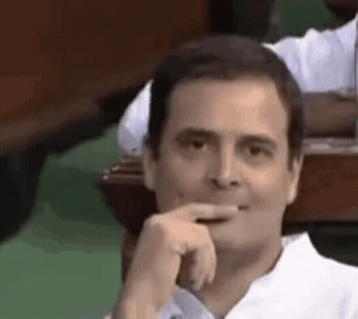 A Man In A White Shirt Is Sitting At A Table With His Hand To His Chin . GIF