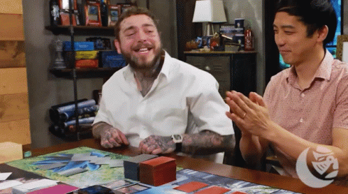 A Man In A White Shirt Is Sitting At A Table With Two Other Men Applauding GIF