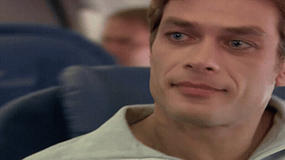 A Man In A White Shirt Is Sitting In A Blue Seat On An Airplane GIF
