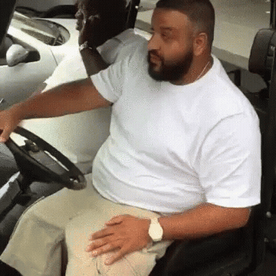 A Man In A White Shirt Is Sitting In A Car Holding The Steering Wheel . GIF