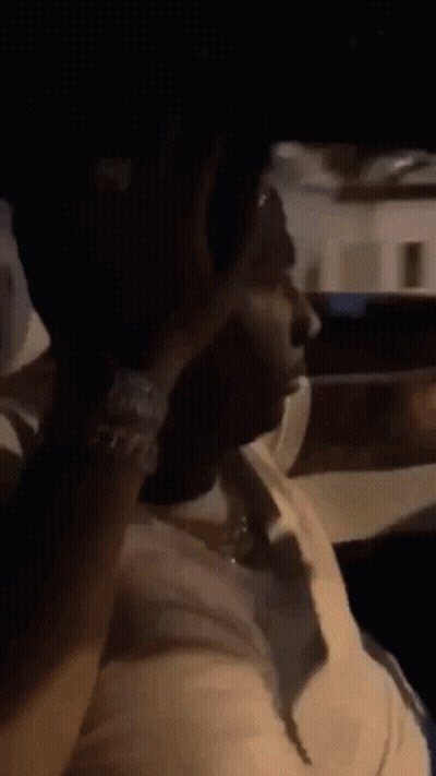 A Man In A White Shirt Is Sitting In A Car Smoking A Cigarette . GIF